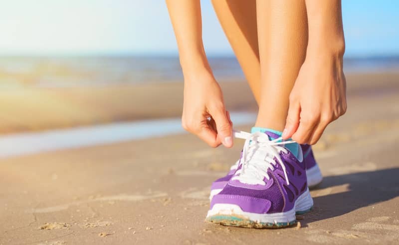 Woman lacing her purple sneakers on the beach